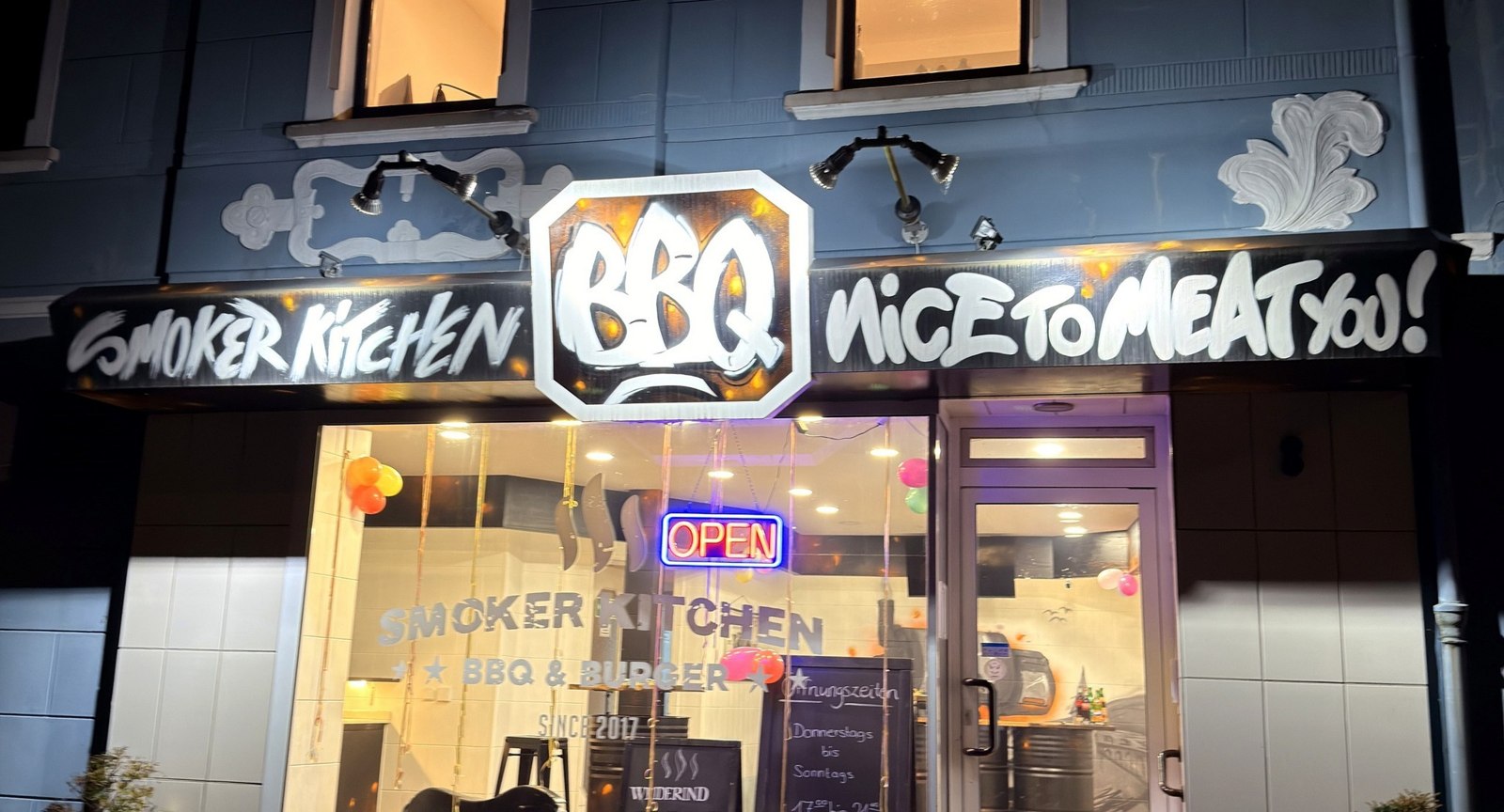 Außenansicht von Smoker Kitchen mit beleuchtetem BBQ-Schriftzug
